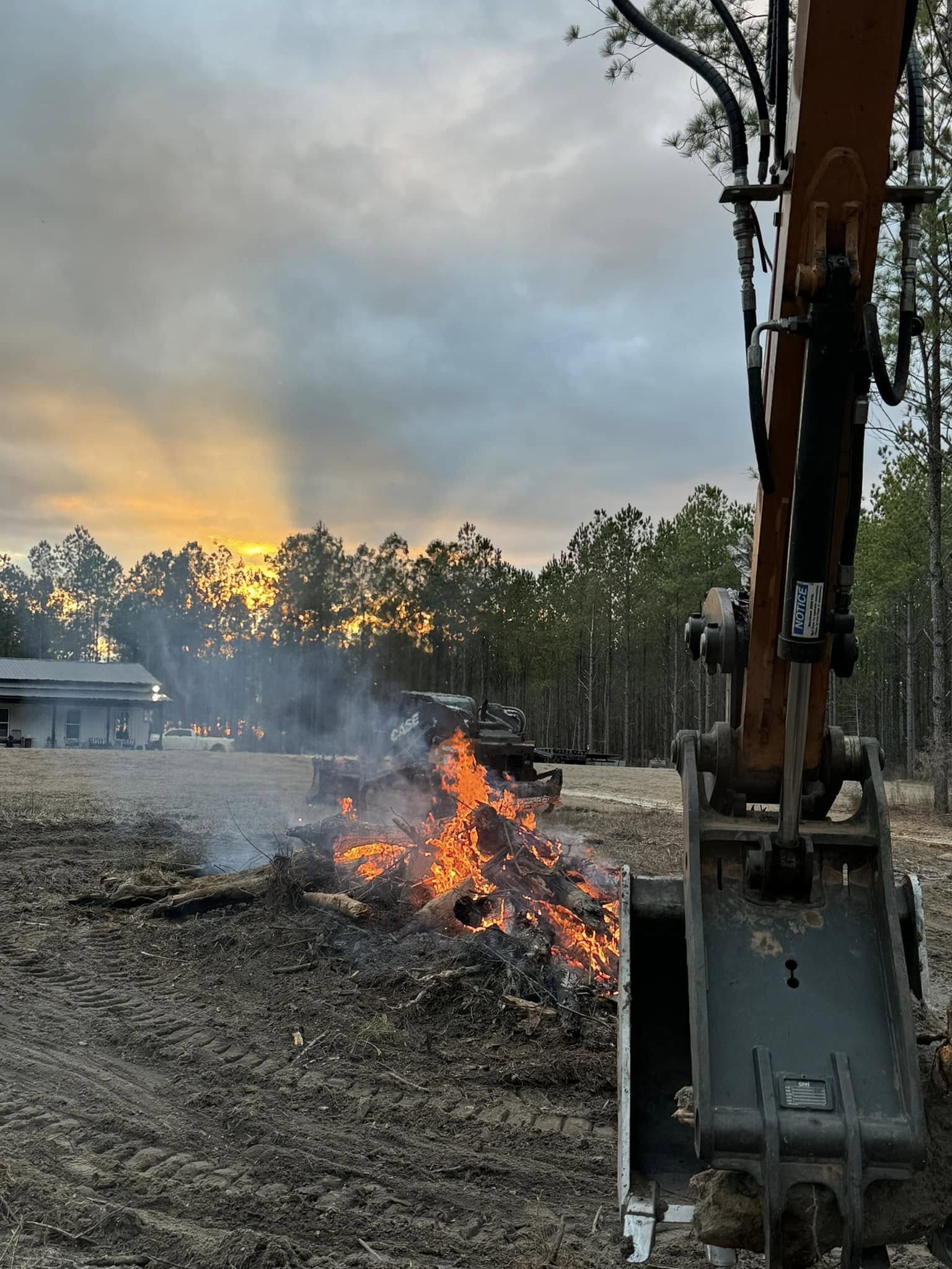 Controlled debris burning at sunset with excavator